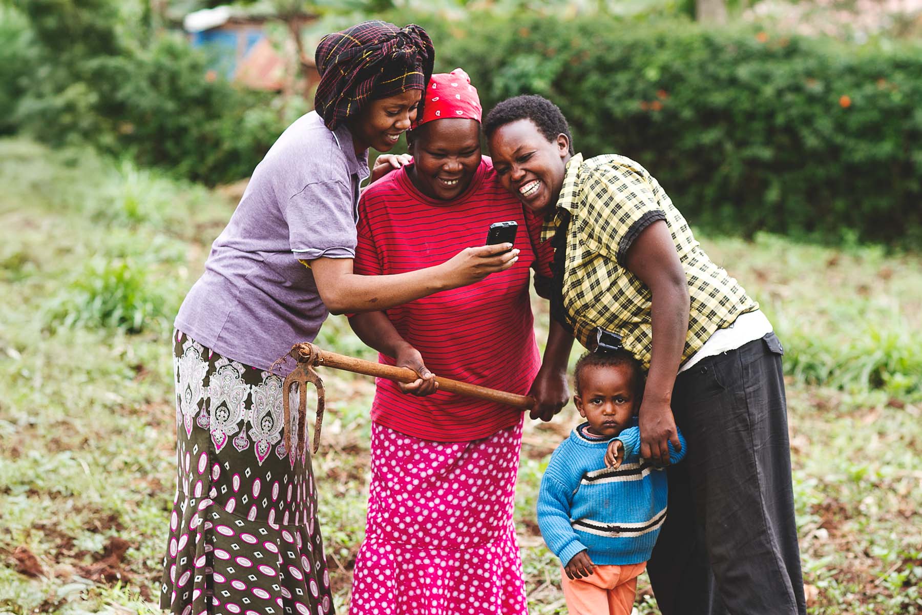 An African family laughs while looking at a smartphone screen in a field.